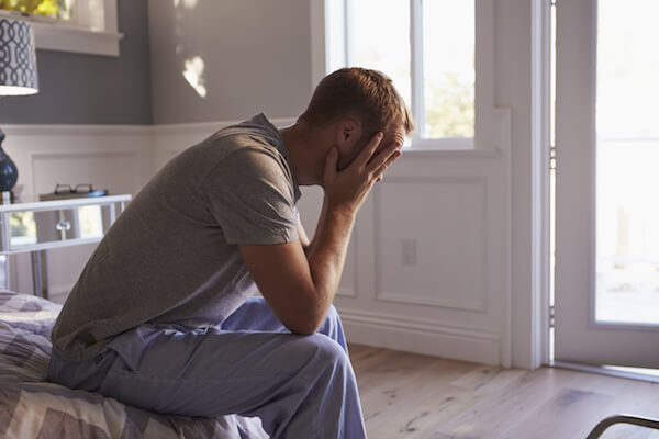 Man Wearing Pajamas Sitting On Bed With Head In Hands