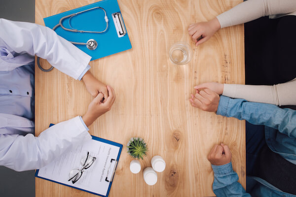 Husband holding wife's hand at doctor's office. Physician ready to examine patient
