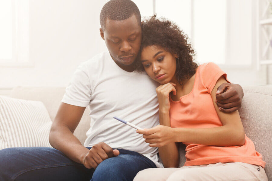 secondary infertility Sad african-american couple after negative pregnancy test result, sitting on couch at home, copy space