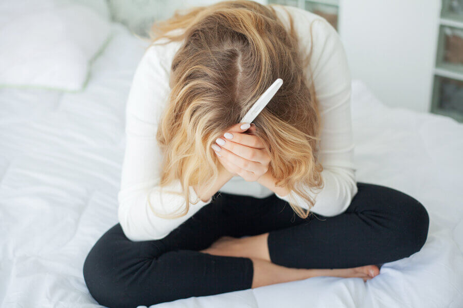 female infertility Positive pregnancy test. Young woman feeling depressed and sad after looking at pregnancy test result at home.