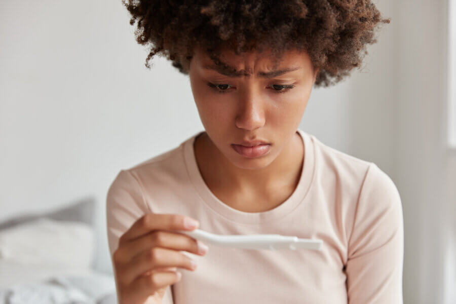 hypothyroidism Desperate sad unhappy black woman looks at pregnancy test, being discontent with result, isnt ready to have baby, poses against domestic interior. People, ethnicity, maternity and fertility concept