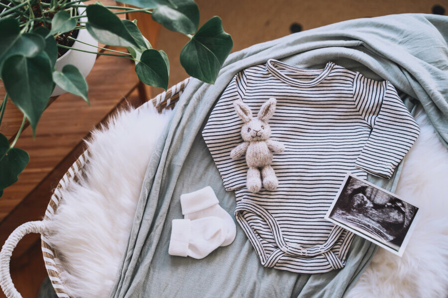 Intracytoplasmic Sperm Injection Baby changing basket with ultrasound image, baby bodysuit, knitted rabbit toy. Still life of child products. Newborn background. Minimalist style photography of baby shower, pregnancy announcement.