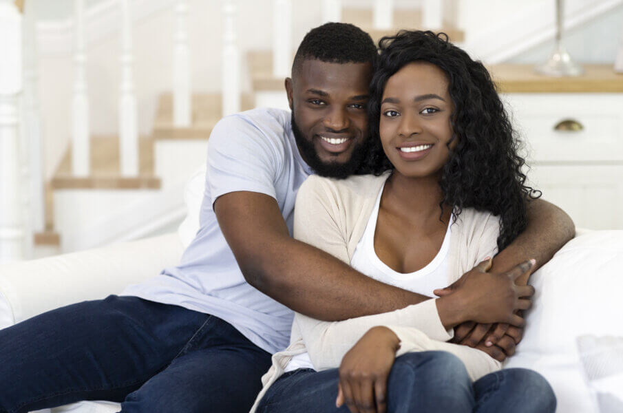 embryo assisted hatching Smiling black husband and wife embracing and looking at camera while sitting on sofa