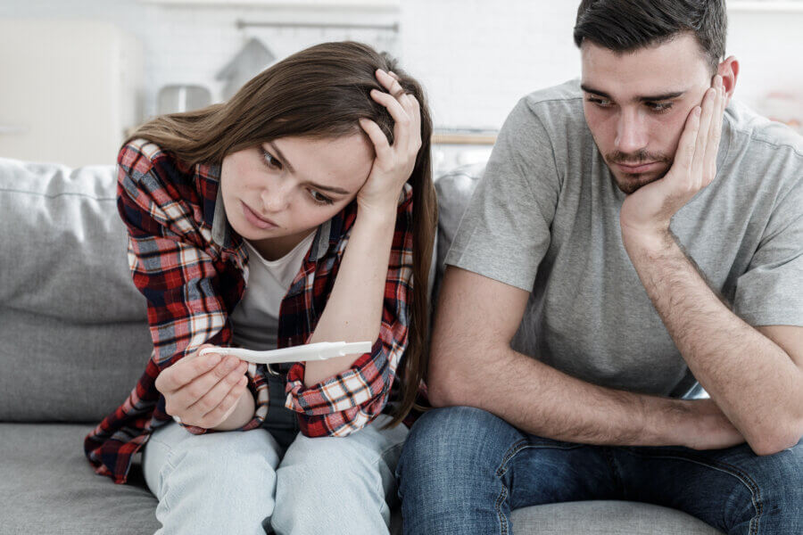 reproductive help Young couple worried because of positive result of pregnancy test, looking upset